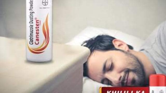 A man is sleeping peacefully on a bed next to a bedside table with a red and white can of Canesten Clotrimazole Dusting Powder. Text reads: "Khujli Ka First-Aid" and "For an Itch-Free Sleep.